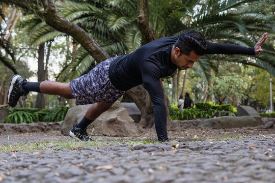 Entrenador mexicano realizando rutina de plancha con extensión cruzada en parque deportivo - perfil 2