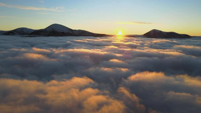 Aerial view of vibrant sunrise over white dense fog with distant dark peaks of Carpathian mountains on horizon