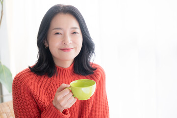 コーヒーを飲みながらくつろぐアジア人（日本人）女性　コピースペースあり　正面　カメラ目線