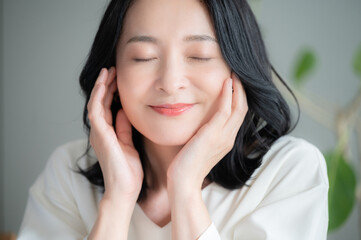 お肌の調子を気にして目を閉じる美しいアジア人(日本人）女性 クローズアップ　正面　カメラ目線