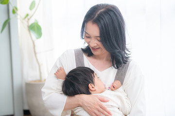 Obraz na płótnie Canvas 赤ちゃんを白い綺麗な部屋で抱っこする笑顔の美人ママ 　ズームコピースペースあり 