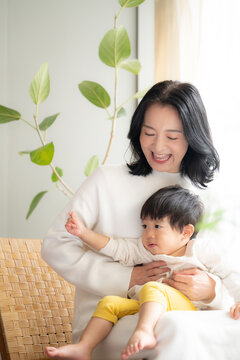 赤ちゃんを白い綺麗な部屋で抱っこするとても幸せそうなママ　コピースペースあり　縦写真	