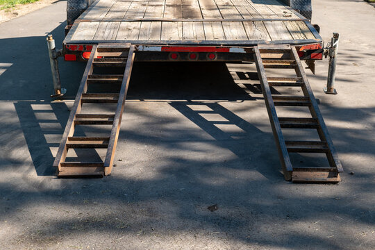 Ramps attached to a truck for loading a vehicle of machine onto the flatbed trailer as it sits parked on the asphalt of the street.