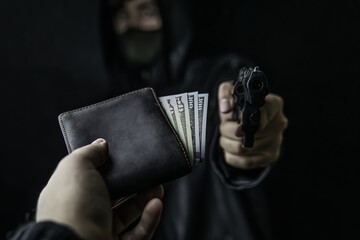 Man's hand holds out purse of money to robber with gun. Armed robbery. Firearm is pointed at camera. Criminal in hood and mask. Assault on unarmed man. Hundred and fifty dollars in open wallet.