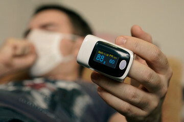 oxygen saturation of the blood. pulse oximeter on a mans finger. A patient in a medical mask...