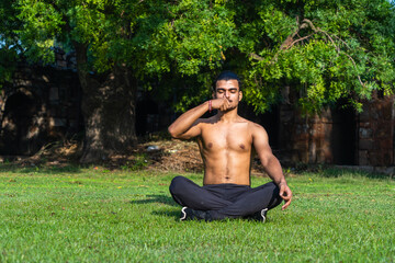 young muscular man doing yoga on grass on a sunny day