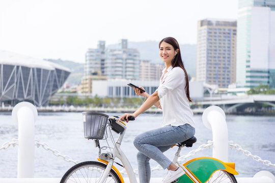 Smiling girl in headphones, holding smartphone and riding bicycle in the park