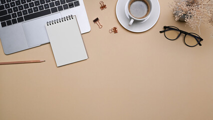 Comfortable workspace with laptop computer, notepad, glasses and coffee cup on beige background.