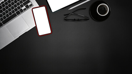 Smart phone with blank screen laptop computer and coffee cup on black table.