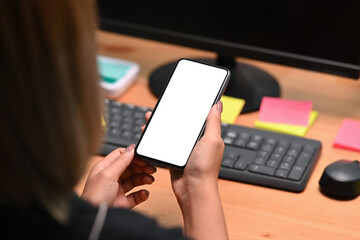 Over shoulder close up view of young woman holding smart phone with white screen.