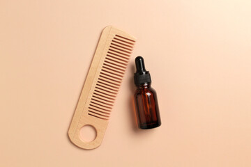 Hair care oil and wooden comb on beige background