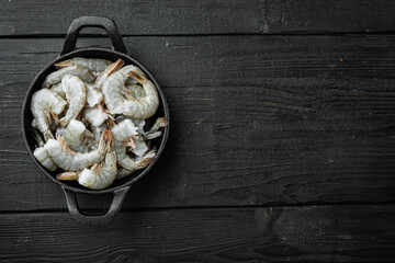 Black raw tiger shrimps, in cast iron frying pan, on black wooden background, top view flat lay,...