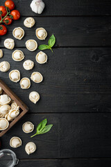 Obraz na płótnie Canvas Italian tortellini with fresh ricotta leaves and tomatoes, on black wooden table background , top view flat lay , with copyspace and space for text