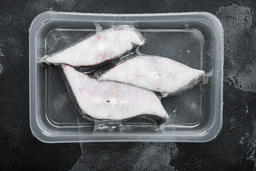 Halibut iced fillet plastic pack, on black dark stone table background, top view flat lay