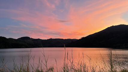 Beautiful colorful sunset. Panorama of sky, hills and lake. Amazing pattern of clouds and pink orange glow of sun at the heaven. Reflection on the surface of the water. Landscape. Violet sundown.