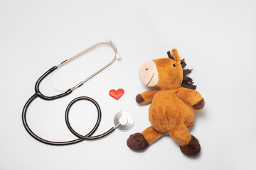 A red heart and a stethoscope or phonendoscope with a plush toy on a white background: pediatric cardiology, blood donor for children. Background of Health and Medicine