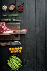 Cooking meat background. Raw tomahawk steak, with spices and herbs for cooking, with grill ingredients, on black wooden table background, top view flat lay, with copy space for text