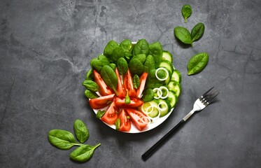 Salad with spinach, fresh cucumbers, tomatoes and onions with cutlery on a gray concrete background. Healthy vegetarian food. View from above. Copy space