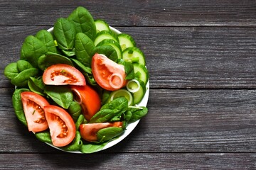 Salad with spinach, fresh cucumbers, tomatoes and onions on a wooden background. Healthy vegetarian food. View from above. Copy space