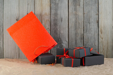 Gifts in black boxes tied with a red ribbon and a red shopping bag stand on craft paper against a wooden background