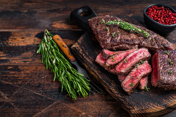 Grilled sliced skirt beef meat steak on a cutting board with herbs. Dark wooden background. Top...