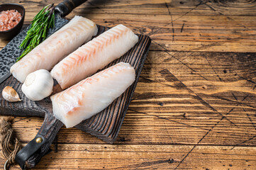 Fresh Raw cod loin fillet steaks on wooden board with butcher knife. wooden background. Top view. Copy space - obrazy, fototapety, plakaty