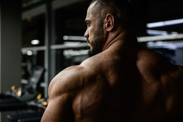 strong young bearded male trainer with muscular back shoulders in night sport fitness gym