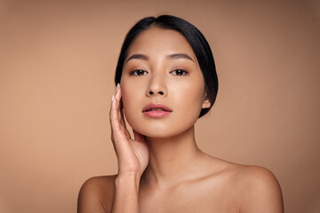 Closeup headshot portrait of young nude asian woman touching smooth clean fresh cheek skin looking at camera. Aesthetic cosmetology and dermatology, face care and facial treatment concept - Powered by Adobe