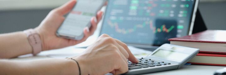 Woman is counting on calculator and holding mobile phone with charts of cryptocurrency rate closeup