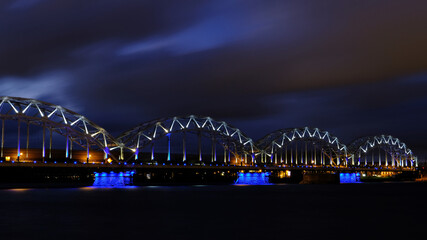 Reflection of night lights at dawn on the Daugava in Riga against the background of the railway bridge