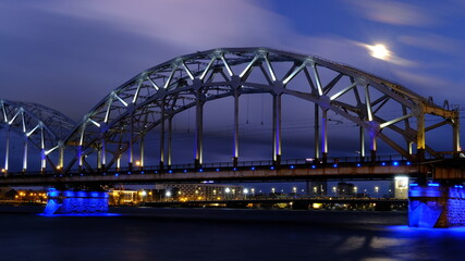 Obraz na płótnie Canvas Reflection of night lights at dawn on the Daugava in Riga against the background of the railway bridge