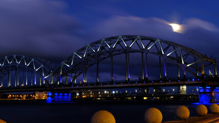 Reflection of night lights at dawn on the Daugava in Riga against the background of the railway bridge