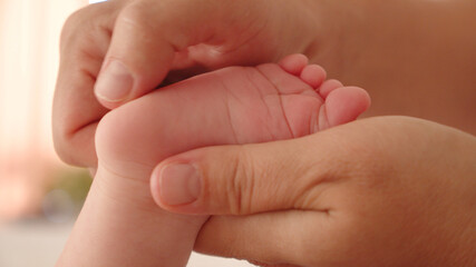 Mother doing massage for her healthy infant baby. Small caucasian newborn laying on his belly while his mother is performing a massage for his small feet and developing toes. .