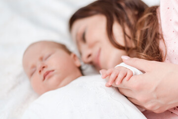 Fototapeta na wymiar Young beautiful woman holding small hand of her sleeping baby daughter in bedroom