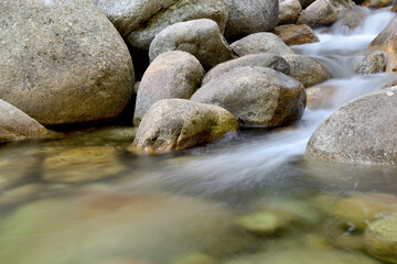 Naklejka na ściany i meble river water flowing between rocks in slow speed shooter