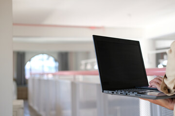 Man typing on a laptop computer while sitting at a white office work table with a cup of coffee and office equipment.