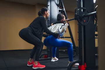 Fototapeta na wymiar Young woman working out legs with barbell In gym with personal female trainer. Squat Exercise 