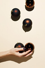 Woman's hand holding a shiny bronze colored Christmas tree ball on a pastel beige background. New Year elegant ornaments. Creative glamourous Xmas composition. Flat lay.