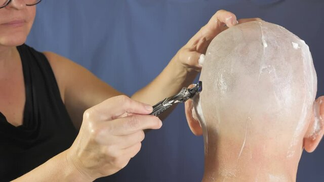 The blade moving back and forth on the side of the bald head of the man with the cream on the other side.