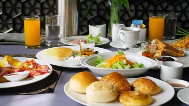 Table with food and drinks for dinner, lunch or brunch in restaurant or cafe. Hotel or resort buffet breakfast concept. Delicious meals, salad, orange juice, fresh pastry, bakery, coffee. Slow motion.