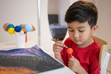 4 years old preschooler making a 3D solar system on a list of paper. Homeschool education. Handmade Astronomy objects.