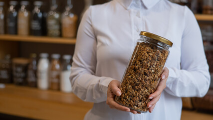 A woman holds a glass jar of granola in an eco friendly store. The concept of a grocery store without plastic disposable packaging