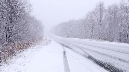 Empty car road during snowfall in winter, poor visibility for drivers.