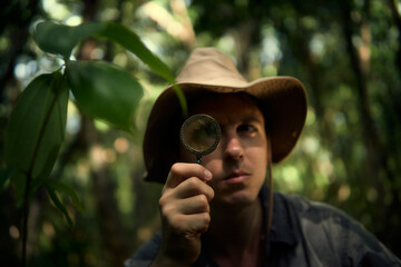 A guy with a magnifying glass and a hat is exploring the jungle. Travel, adventure, expedition.