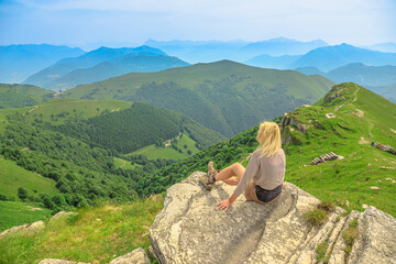 Tourist woman on a rock on top view of Monte Generoso or Calvagione Swiss mount. Aerial skyline of Lugano lake of Ticino canton. Top of cog train station in Mendrisio district, Switzerland.