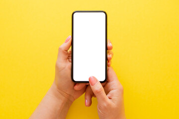 Person holding blank mobile phone in both hands on yelloe background