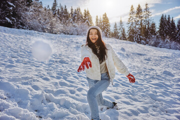 Winter woman playing in snow throwing snowball at camera smiling happy having fun outside on...