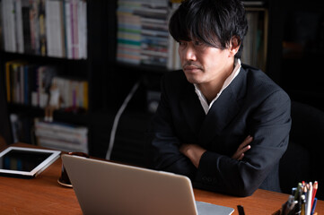 腕を組んで考え事をするハンサムなアジア人（日本人）ビジネスマン男性　左にコピースペースあり