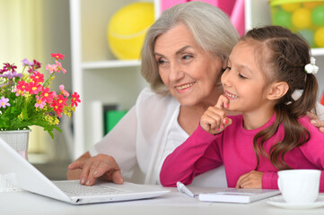portrait of happy grandmother and granddaughter using laptop