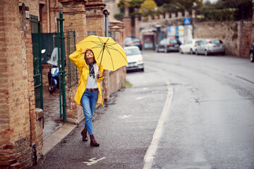 A young girl with yellow raincoat and umbrella is walking the city on the rain. Walk, rain, city - obrazy, fototapety, plakaty